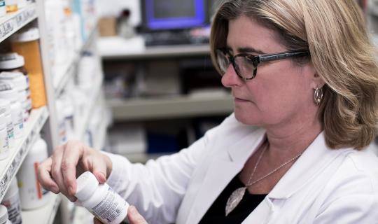 Pharmacist examining a pill bottle behind the pharmacy counter