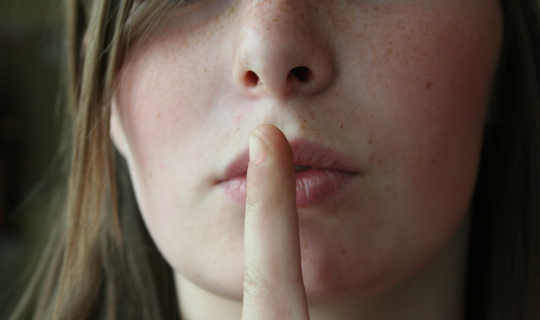 A woman holding her index finger up to her lips to hush someone