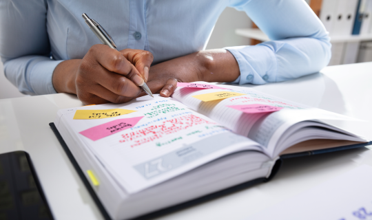 A woman writing out a social media content schedule in a daily planner notebook