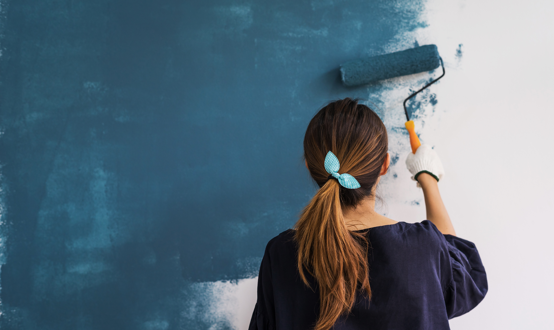 A woman painting the walls of her pharmacy blue using a paint roller
