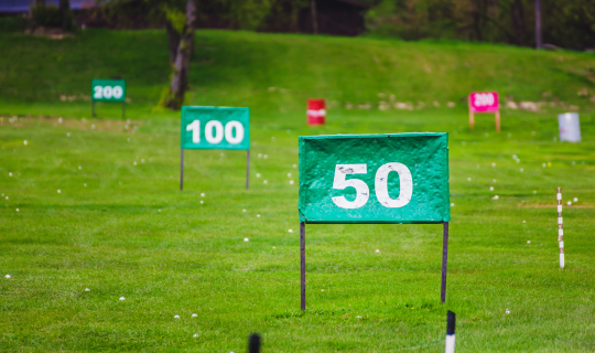 Distance markers laid out on a driving range with golf balls strewn across the grass