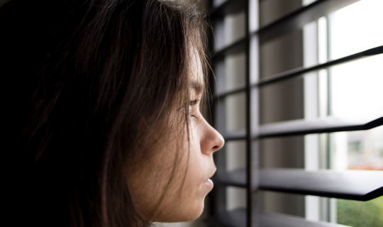 A woman peeking through window blinds