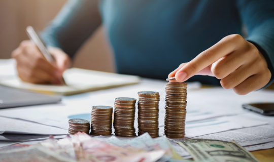 A woman stacking coins into five towers increasing in size from left to right as she takes notes on a sheet of paper