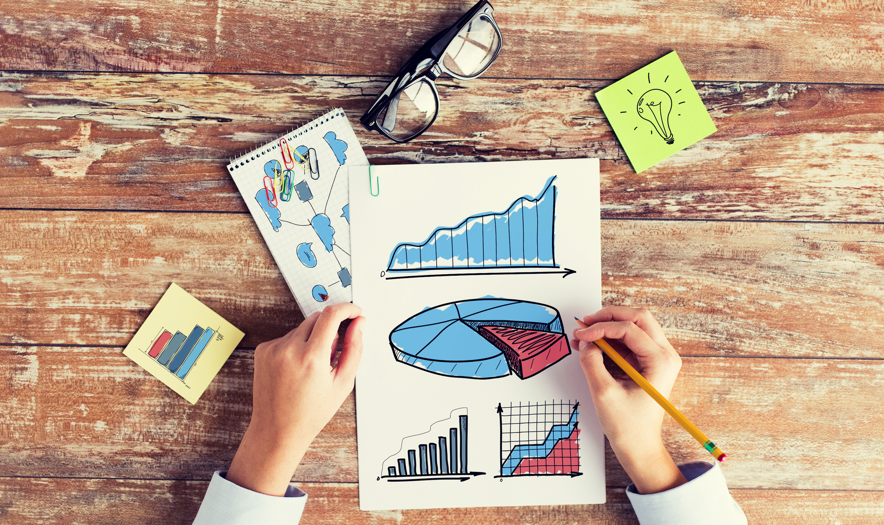 A person reviewing a variety of colorful charts set out on a rustic table