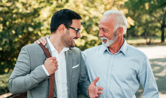 A father with his arm around his son as they walk and talk