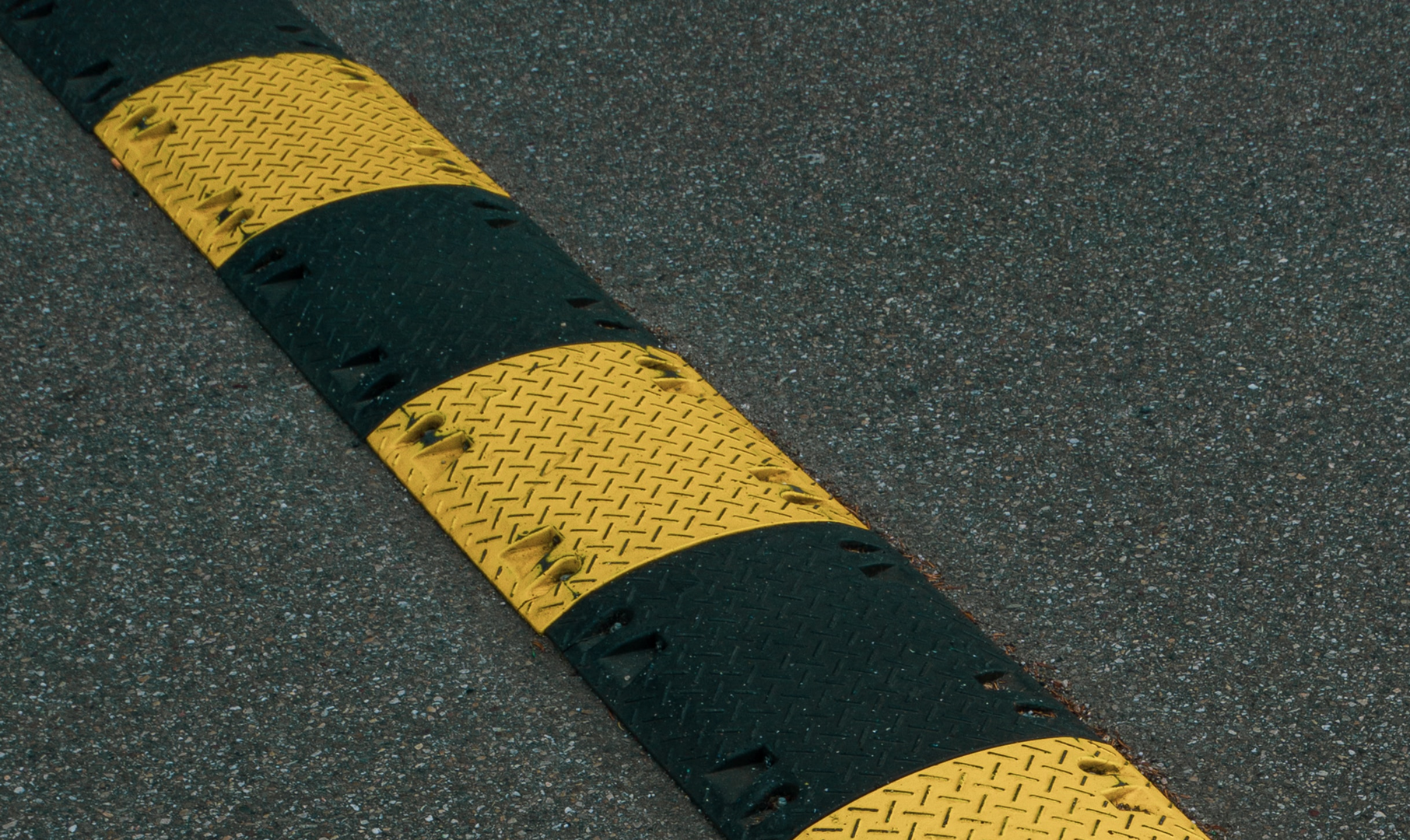 A yellow and black striped speed bump on asphalt