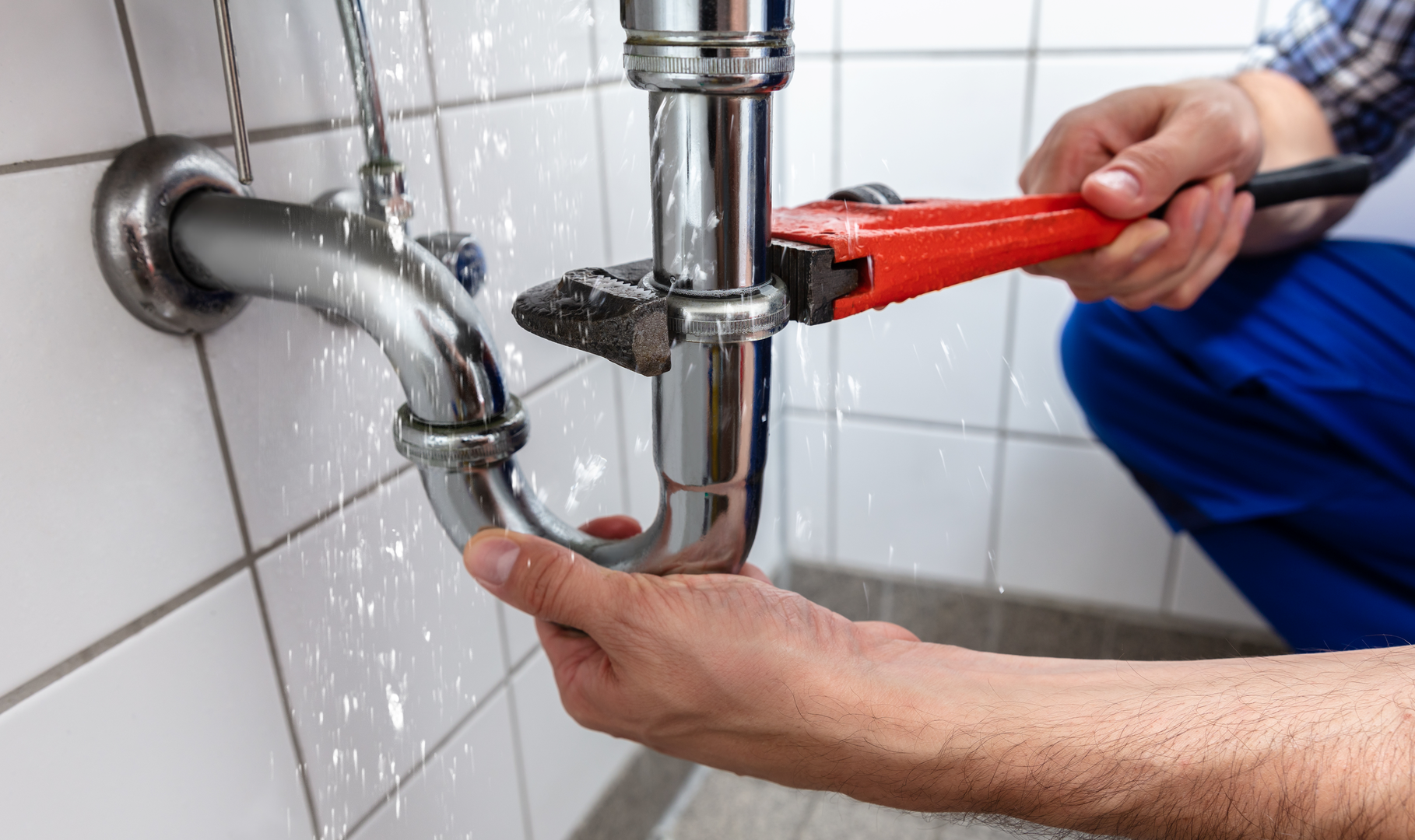 A plumber using a wrench to fix a leaking pipe under a sink